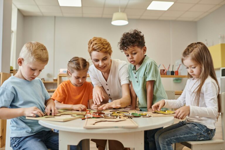 smiling teacher playing with multiethnic kids near game on table in montessori school